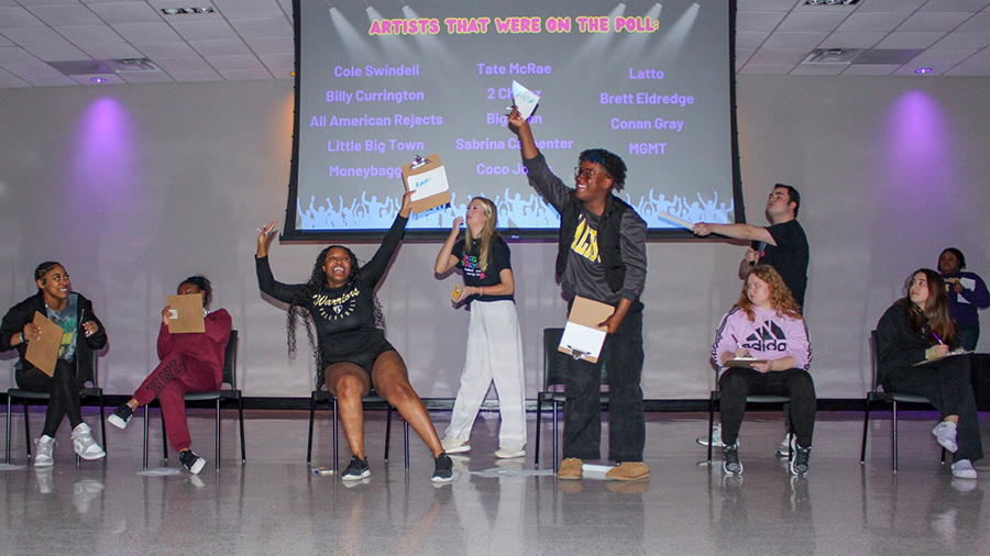 Students sitting on chairs and standing as they play an interactive game.