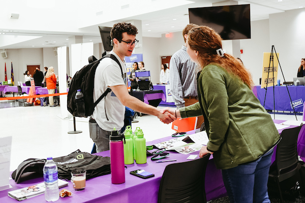 Student shacking hands with a company spokesperson during a career fair.