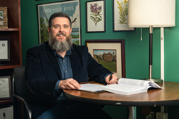 Dr Jonathan Wiley posing for a photo while sitting at a table taking notes from a text book.