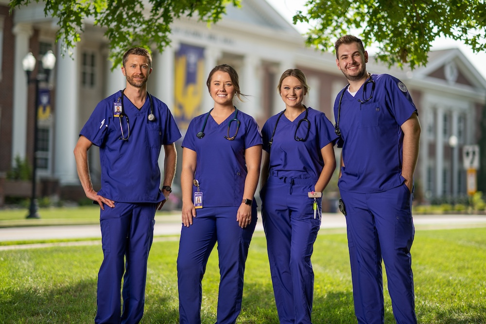 Four nurses standing in purple scrubs under a tree