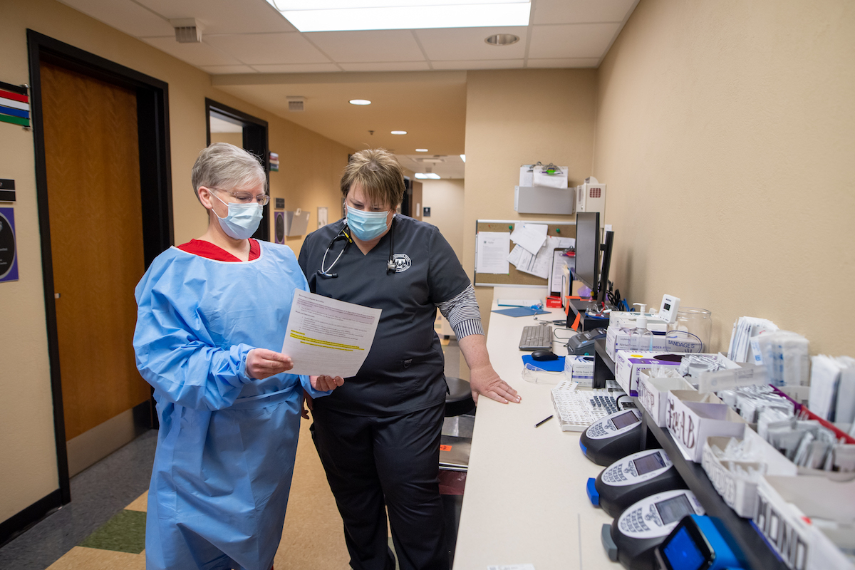 Two masked nurses stand looking at a paper in a lab